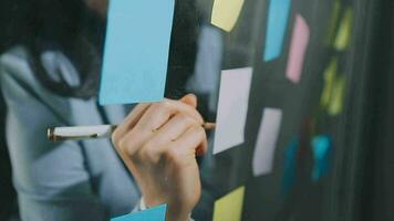 Young asian business woman working on project plan using sticky papers notes on glass wall, people meeting to share idea, Business design planning concepts. video