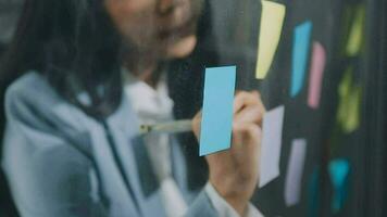 Young asian business woman working on project plan using sticky papers notes on glass wall, people meeting to share idea, Business design planning concepts. video