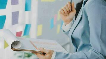 Young asian business woman working on project plan using sticky papers notes on glass wall, people meeting to share idea, Business design planning concepts. video