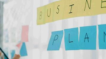 Young asian business woman working on project plan using sticky papers notes on glass wall, people meeting to share idea, Business design planning concepts. video