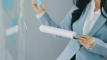 Young asian business woman working on project plan using sticky papers notes on glass wall, people meeting to share idea, Business design planning concepts. video