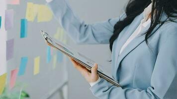 Young asian business woman working on project plan using sticky papers notes on glass wall, people meeting to share idea, Business design planning concepts. video