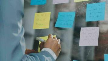 Young asian business woman working on project plan using sticky papers notes on glass wall, people meeting to share idea, Business design planning concepts. video