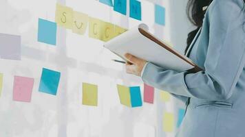 Young asian business woman working on project plan using sticky papers notes on glass wall, people meeting to share idea, Business design planning concepts. video