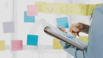 Young asian business woman working on project plan using sticky papers notes on glass wall, people meeting to share idea, Business design planning concepts. video