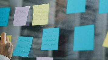 Young asian business woman working on project plan using sticky papers notes on glass wall, people meeting to share idea, Business design planning concepts. video