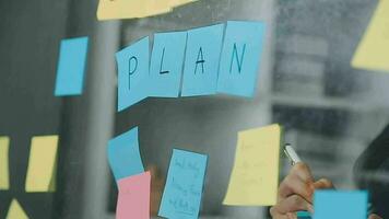 Young asian business woman working on project plan using sticky papers notes on glass wall, people meeting to share idea, Business design planning concepts. video