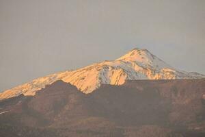 a mountain with snow on top at sunset photo