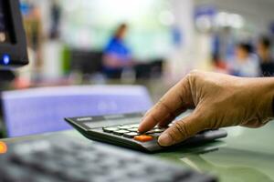 Close-up a man's finger pressing a calculator on a glass table in an office To calculate bank interest money for customers who need a loan, blurred background, and has bokeh, the select focus at hand. photo