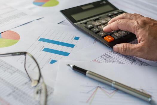 A businessman is calculating numbers with a calculator. concept financial accounting, close-up a calculator on a desk, check account number on paper, lots of numbers, graph, blurred background photo