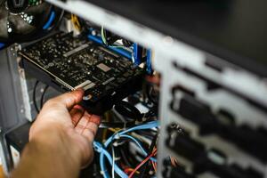 A technician's hand holds the graphics card to fix it. The VGA card is damaged causing the computer to fail. The display card does not display a PC screen. Close up photo and selective focus on hand.