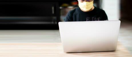 The masked man was working at home using a laptop, communicating via the internet with a customer during the coronavirus or COVID-19 outbreak, and as a preventive measure. copy space on left put text photo