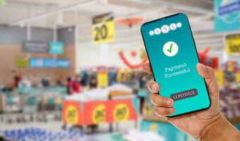 A man's hand holds a smartphone on screen with message Payment Successful in a supermarket. Concept of financial transactions with mobile devices. Closeup, money, transfer, online. blurred background photo