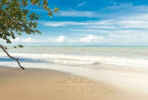 New Year 2023 Concept. inscription is a 2023 number on sand beach. Sandy beach and sea wave beautiful background. Write letters by hand on the beach. change year 2022 to year 2023 on sand of beach photo