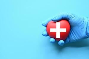 A red cross is a symbol of medical health. Hand holding a heart and on a blue background. Copy space for the text and contents. red cross CPR, World heart day, world health day, blood organ donation photo