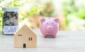 Model wooden house on wood table, concept, business, finance, banking, saving, real estate, investment. copy space on right for the design. nobody, no people, blur pink pig piggy bank, and background photo