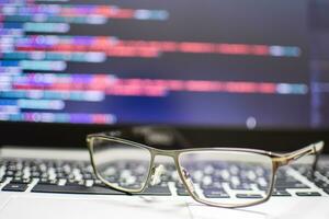 The programmer's glasses put on the keyboard laptop to relax after long coding for application creation and website design for businesses. Take a close-up shot and blurred background with source code photo