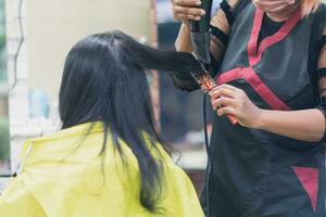 professional woman hairdresser wearing face mask holding hair dryer and hair styling client woman indoor salon, Business hair care has tool haircut to service haircut to a customer, selective focus photo