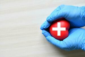 A red cross is a symbol of medical health. Hand holding a heart and on a wooden desk. Copy space for the text and contents. red cross CPR, World heart day, world health day, blood organ donation photo