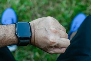 The man was tired and sat down to relax, looking at the smart watch after jogging. It's a close-up photo with a blurred background.