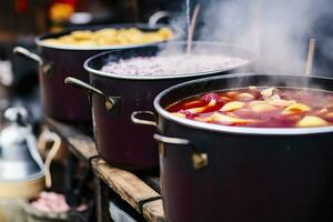 Beverages fruits and berries hot mulled wine in pots with steam in street food market. Generative AI photo