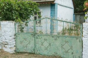 The gate to the house is decorated with a pattern of metal. Old abandoned house in the village Old iron gate in the yard of a country house. Green metal gate. photo