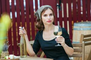 Beautiful young woman drinking white wine on the terrace of a restaurant. Relaxing after work with a glass of wine. Single woman having fun. photo