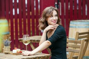 hermosa joven mujer Bebiendo blanco vino en el terraza de un restaurante. relajante después trabajo con un vaso de vino. soltero mujer teniendo divertida. foto