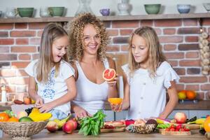 Mother and daughters cooking together in the kitchen. Healthy food concept. Portrait of happy family with fresh smoothies. photo