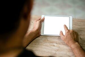 Hand of a man touching tablet device with a blank white screen on the desk wood in the work at home, take a closeup photo, copy space, clipping path, blurred background. photo