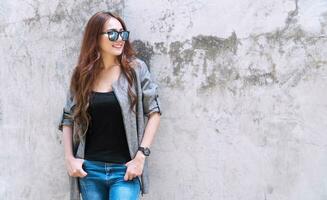 Professional business of young woman wearing sunglasses looking at something while standing on concrete walls background with copy space. photo