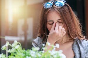 Tired young businesswoman massaging nose bridge feeling eye strain or headache trying to relieve pain. Overworked young woman have migraine feeling straining her eyes while sitting in garden. photo