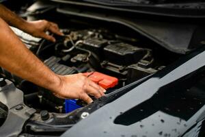 Closeup, The hands of a male technician are using a tool to replace the car battery, parked at home. Black car, the battery is damaged. Man is checking the battery of a black car with no power. photo