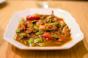 Spicy curry with shrimp paste and shrimp paste on a white plate on a wooden table. Seafood among Thai people is very popular. Take close-up and slope view. Selective focus. Blurred background. photo