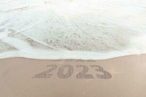 change new year of 2023 on sand of beach. New Year 2023 Concept. inscription is a 2023 number on sand beach. Sandy beach and sea wave beautiful background. Write letters by hand on the beach. photo