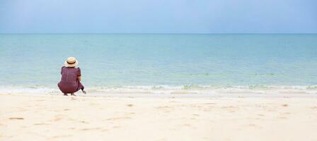 A single woman sits on the beach and looks out onto the clear sea. The weather is clear. copy space on right for design or content. blurred background photo