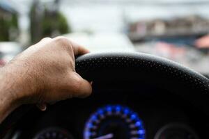 un hombre conducción un izquierda mano a sostener el direccion rueda a controlar el coche cuidadosamente mientras tráfico congestión, tiene copyspace en parte superior para entrada texto, tomar un de cerca disparo, borroso antecedentes foto