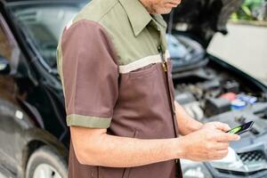 Technician holds smartphone to watch the battery function monitor. Mobile device screen show battery status. Concept of using digital technology devices for car fix. Selective focus. Blur background photo