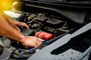 Closeup, The hands of a male technician are using a tool to replace the car battery, parked at home. Black car, the battery is damaged. Man is checking the battery of a black car with no power. photo