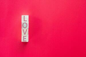 Take a close-up shot. The LOVE letters on the wooden cube are arranged vertically on a red background. Concept of Love Day or Valentine Day photo
