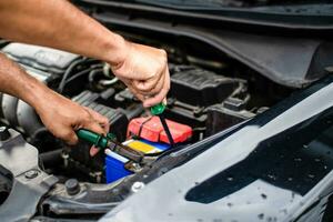 Closeup, The hands of a male technician are using a tool to replace the car battery, parked at home. Black car, the battery is damaged. Tools have pliers and screwdrivers. photo