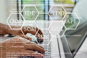 Abbreviations that every programmer should know, such as OOP, SCM, VCS, WYSIWYG, GUI, API, IDE, TDD, SDK. Programmers sit and write programs with their laptop computers. Close up, Blurred background photo