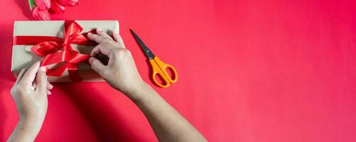 A woman packaging gift boxes and tied with red ribbons on a red background. the concept for Valentine's Day, Christmas, party, birthday. Has copy space on right for design or text. Selective focus. photo