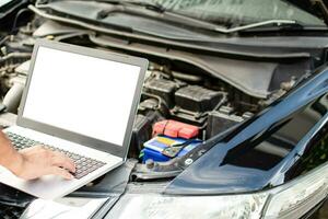 Closeup, A man's hand typing on a laptop computer keyboard to check the operation of the car engine in the garage. The engine of a car does not start. A notebook computer is a white screen and a blank photo