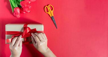 un mujer embalaje regalo cajas y atado con rojo cintas en un rojo antecedentes. el concepto para enamorado día, Navidad, fiesta, cumpleaños. tiene Copiar espacio en Derecha para diseño o texto. selectivo enfocar. foto