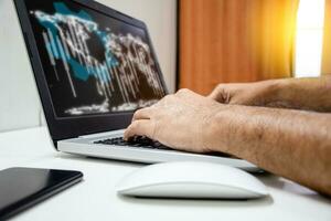Take a close-up of male hands and laptops with a white world, graph, and cogs on screen. A notebook computer, white mouse, and black phone on a white table. daylight and blurred background. photo