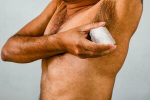 Men apply alum to their armpits to eliminate body odor after they finish showering. Alum helps deodorize men's armpits. The male hand holds alum and rubs the armpit area to eliminate the bad smell. photo