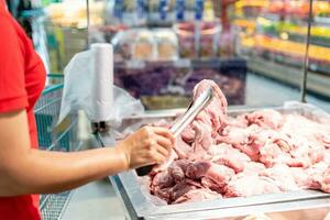 A woman holds and looks at fresh pork to buy quality pieces at the fresh produce section of the supermarket. Close up, Selective focus, Blurred background, Copy space for text or design. photo