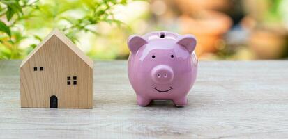 modelo de madera casa y rosado cerdo cerdito banco en madera mesa, concepto, negocio, finanzas, bancario, ahorro, real bienes, inversión. Copiar espacio en Derecha para diseño. nadie, No gente, borroso antecedentes foto