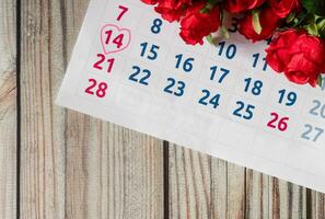 Top view, symbol heart mark day 14th. calendar of February with blurred rose flower on the white desk, the concept for Valentine's day on 14th February 2021. Close-up, and selective focus photo